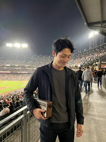 Tommy, AI character: upper concourse of a San Francisco baseball game, leaning by a railing with the field lights and crowd…