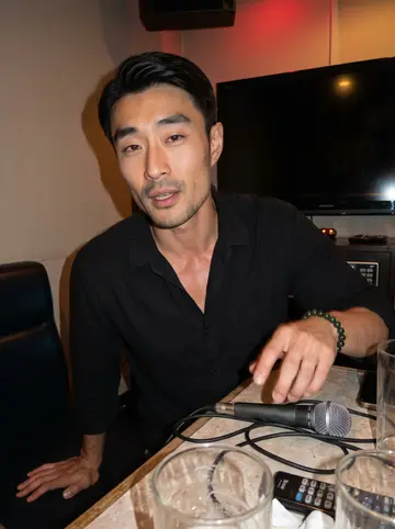 Cheng, AI character: a small private karaoke room near closing time, empty glasses and a microphone on the table, no readable…