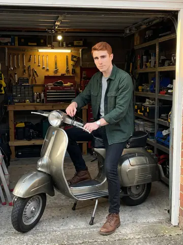 Hamish, AI character: his rented lock-up garage off a quiet Edinburgh lane, a partly restored 1960s Vespa beside a workbench