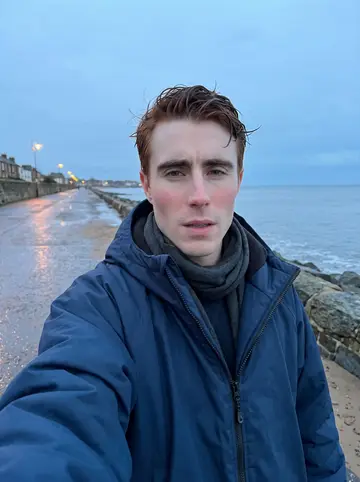 Hamish, AI character: Portobello promenade after a winter sea swim, grey water and low blue sky behind him