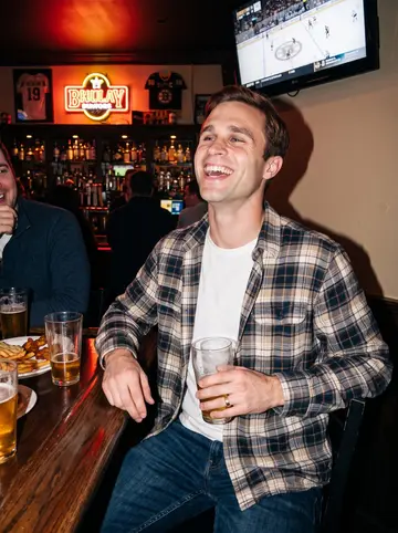 Declan, AI character: the end stool of a crowded Southie pub during a Bruins game, pint glasses and a TV glow behind