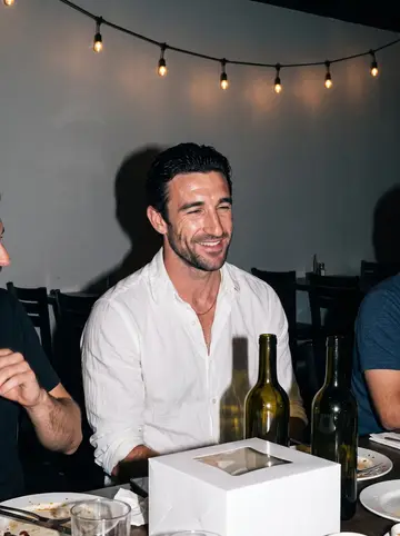 Enzo, AI character: the trattoria after close on his cousin's birthday, long table pushed together, empty wine bottles and a…