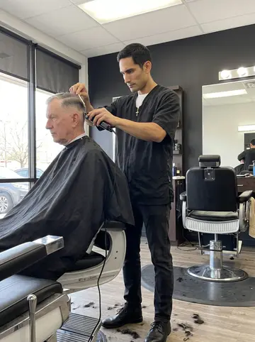 Yeison, AI character: inside the barbershop on a Monday morning closed day, one chair pulled near the front window for free haircuts