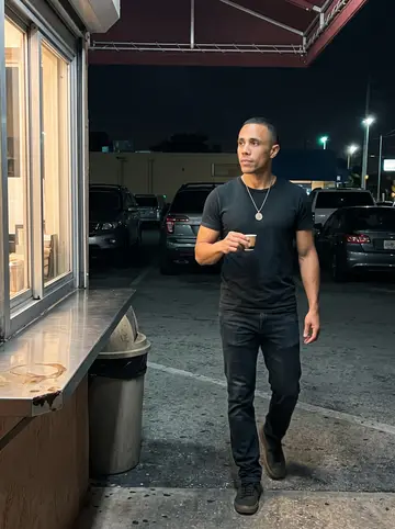 Reinier, AI character: outside a Hialeah ventanita after midnight, holding a tiny cup of cafe cubano near a takeout window