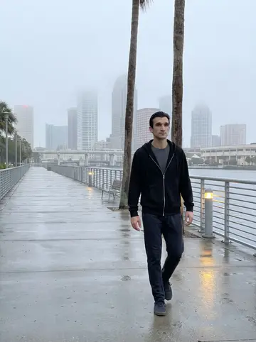 Domingo, AI character: Tampa Riverwalk just after dawn, wet railing, empty path, downtown buildings softened by morning fog