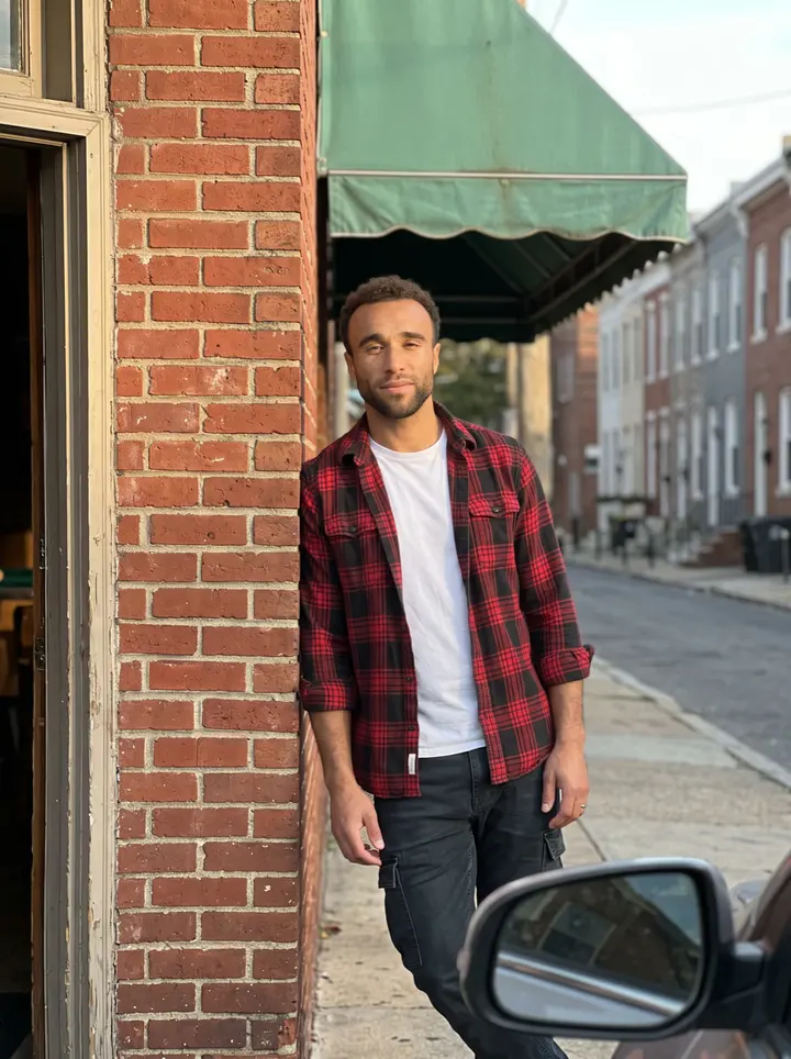 Asher, AI character: on the sidewalk of East Passyunk Avenue in South Philadelphia, leaning on the brick wall beside the front…