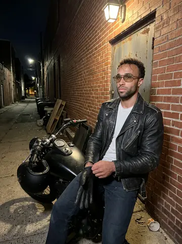 Asher, AI character: a friend's small brick backyard behind a South Philly rowhouse, a charcoal grill, a plastic table with…