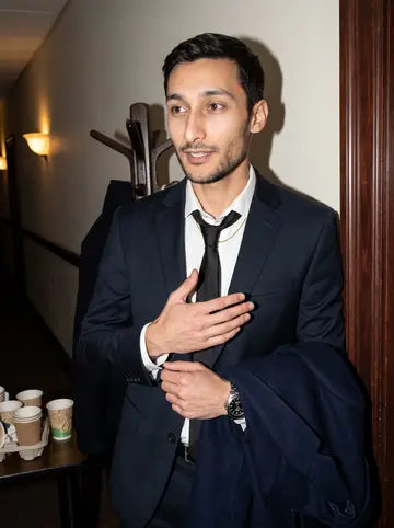 Joel, AI character: a funeral home side hallway after the wake, dark wood trim, coat rack, paper cups on a small table