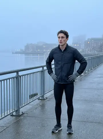 Kurt, AI character: Boston Harborwalk before sunrise, damp pavement, railings and grey water behind him