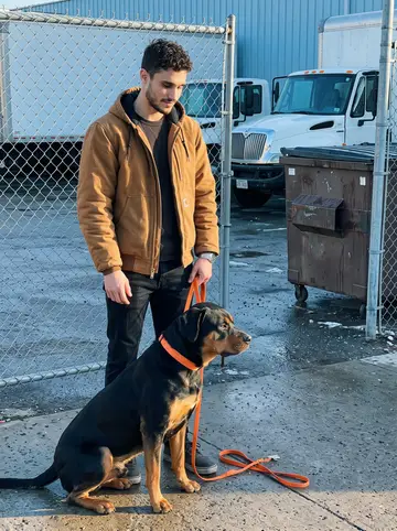 Archie, AI character: inside the chain-link gate of the hauling yard on a clear cold morning, bins and parked trucks in the…