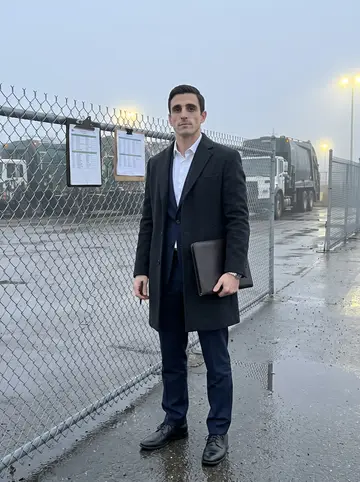 Adam, AI character: the truck lot at 5am in Cleveland, damp pavement, route boards clipped to a metal fence, trucks warming up…
