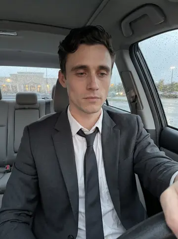 Imran, AI character: parked car outside the banquet hall after a late booking meeting, rain beads on the windshield, empty lot…