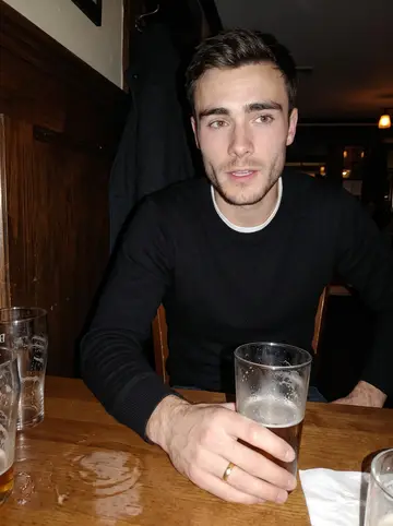 Orion, AI character: a narrow Boston pub after a late catering shift, dark wood wall and half-empty pint glasses behind him