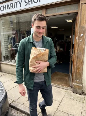 Orion, AI character: outside a charity shop in Cambridge, a paper bag of mismatched teacups in his arms
