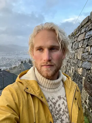 Anders, AI character: the stone wall at a Fløyen lookout above Bergen, wet rooftops and the harbour hazy far behind him