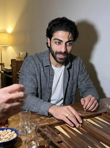 Arman, AI character: the dining table at his parents' house in the evening, a backgammon board, small tea glasses and a bowl of…