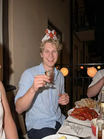 Elias, AI character: a crayfish party on a friend's balcony in Hornstull in August, paper lanterns, plates of crayfish on the…