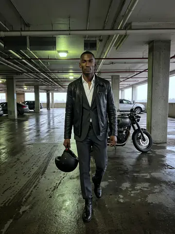 Rotimi, AI character: covered parking deck near the courthouse after rain, wet concrete and his motorcycle parked behind him