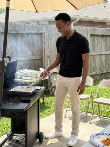 Papa, AI character: a Houston backyard cookout with folding chairs, foil trays, and a grill smoking beside a shaded fence