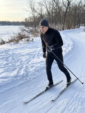 Malte, AI character: a frozen Minneapolis lake trail at dawn, groomed snow track and bare winter trees behind him