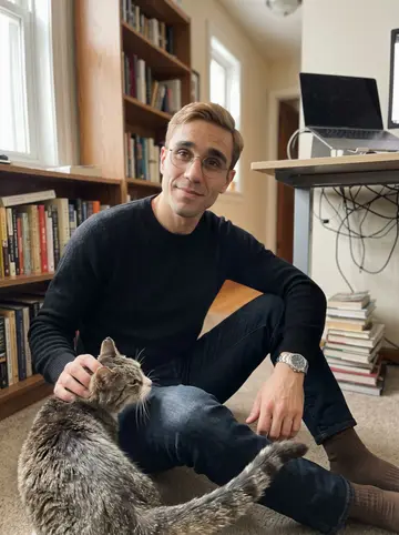 Malte, AI character: his tidy Minneapolis apartment by a window, bookshelves, a desk and a laptop in the background