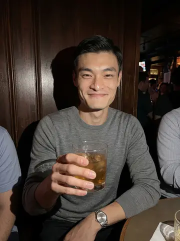 Hiroshi, AI character: a narrow Boston bar after a hospital fundraiser, dark wood wall and half-seen friends cropped around him