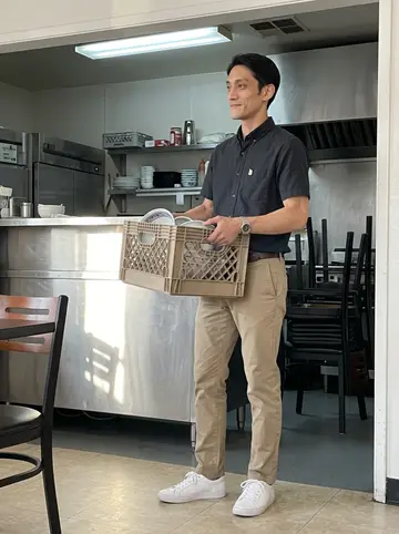 Kenta, AI character: his parents' ramen shop in Gardena after closing, stainless counter and stacked chairs in the background