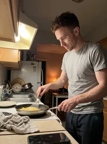 Sylvain, AI character: his small New Orleans apartment kitchen after midnight, pan on the stove and a plate waiting on the counter