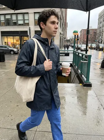 Raphaël, AI character: outside a Boston subway entrance in light rain, heading toward the hospital with traffic behind him