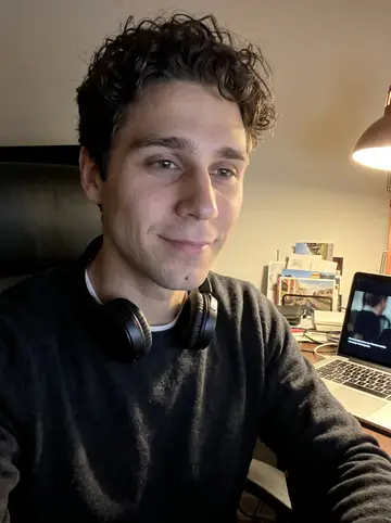 Raphaël, AI character: his apartment desk late at night, an old French film playing on a laptop out of focus with no readable text