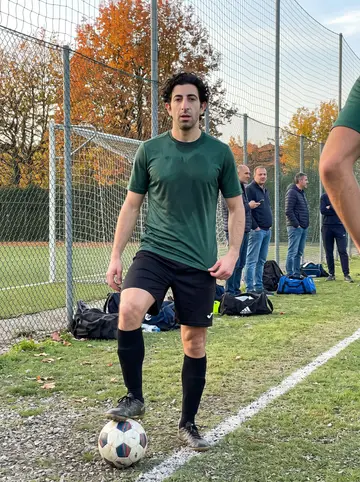 Pietro, AI character: a neighborhood football pitch in Bologna after Sunday play with local fathers, orange leaves along the fence