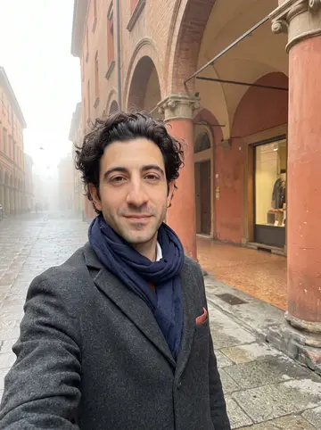 Pietro, AI character: under the Bologna porticoes on a foggy morning walk, terracotta walls and arches receding behind him