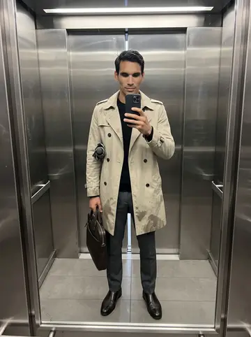 Yunior, AI character: elevator mirror in his Jersey City building on a rainy weekday morning, umbrella tucked under one arm