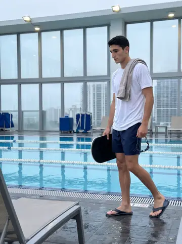 Néstor, AI character: an empty hotel pool deck in Miami at six in the morning, lane ropes still in the water and city buildings…