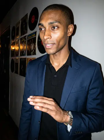 Femi, AI character: a small jazz bar in Harlem, standing near a wall of vinyl sleeves after the set