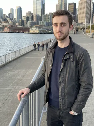 Steven, AI character: a pedestrian overlook near Seattle's waterfront after work, grey-blue water and downtown glass behind him