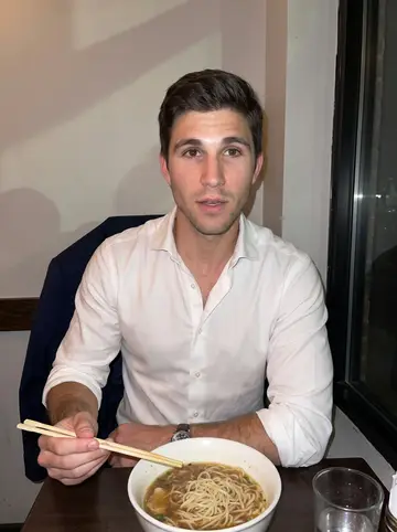 Joseph, AI character: late-night ramen counter in Hoboken after a long day, bowls and water glasses on the counter, dark window…