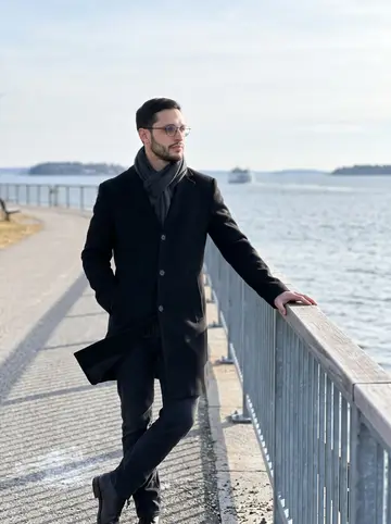 Kelvin, AI character: Eastern Promenade in Portland after a site visit, standing by the railing with Casco Bay and pale winter…