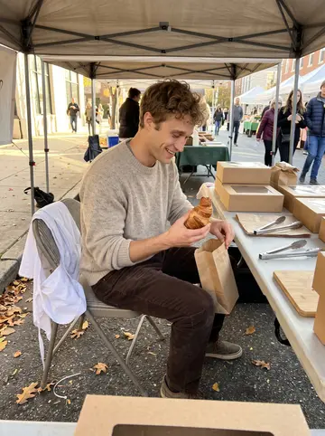 Jacob, AI character: an outdoor bakery stall at a Baltimore farmers market, paper bags and pastry boxes on a folding table