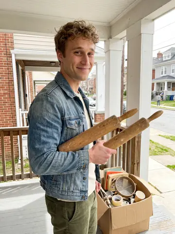 Jacob, AI character: a Baltimore estate sale porch with boxes of kitchen tools and old cookbooks