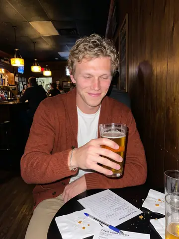 Riley, AI character: a casual Charlotte neighborhood bar during trivia night, a small round table crowded with score sheets and…