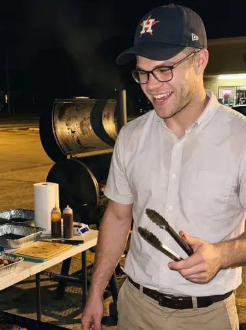 Jarrett, AI character: the pawnshop back lot on a humid Houston Saturday night, borrowed smoker open behind him, folding table…