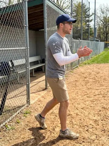 Jarrett, AI character: a Little League field in Montrose during weekend practice, chain-link fence and dugout behind him