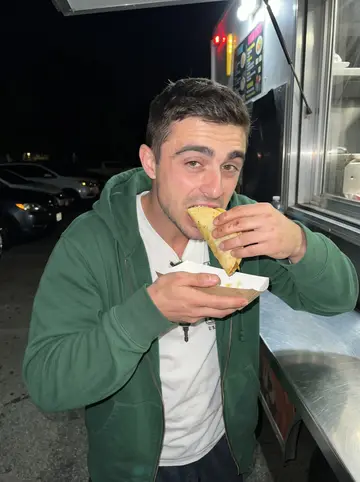 Kobe, AI character: outside a late-night taco truck in East Austin, metal counter and parked cars behind him