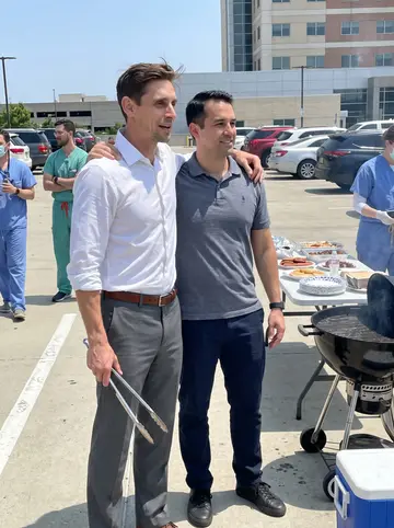 Bruce, AI character: hospital charity cookout in a sunlit staff parking lot, folding tables and coolers behind him