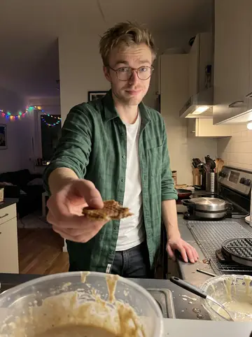 Wouter, AI character: his small apartment kitchen in December, with a waffle iron, cooling rack, and a messy bowl of stroopwafel…