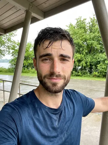 Mykhailo, AI character: under the lakefront trail shelter after a humid run, wet pavement and trees behind him