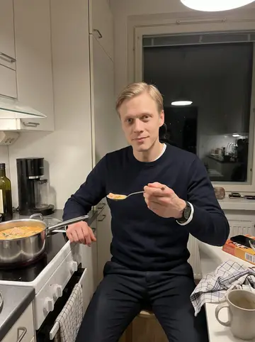 Niko, AI character: compact Helsinki apartment kitchen on a dark winter evening, pot of salmon soup on the stove