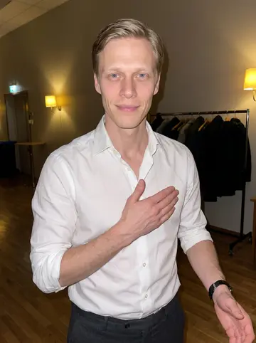 Niko, AI character: small community dance hall after a Finnish tango lesson, wood floor and coat rack behind him