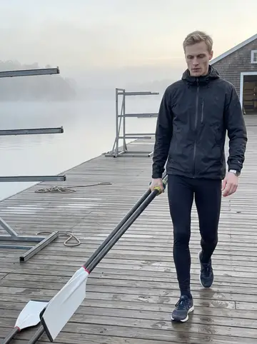 Mykola, AI character: boathouse dock on the Charles at dawn, low fog over the water and empty racks behind him
